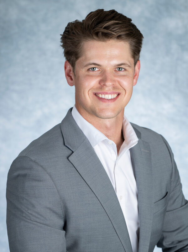 A headshot of Jordan Nolan in a grey blazer.