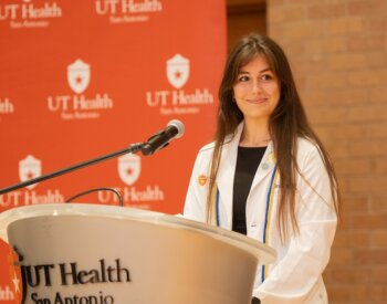 Doctor of Occupational Therapy student Grace McGuire stands at a podium in her white coat.