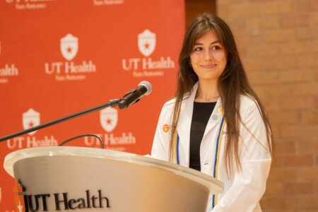 Doctor of Occupational Therapy student Grace McGuire stands at a podium in her white coat.