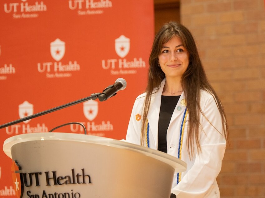 Doctor of Occupational Therapy student Grace McGuire stands at a podium in her white coat.