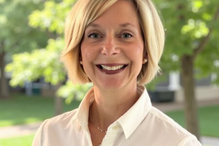 Woman smiles at camera, stands in front of trees.