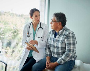 A female physician talks to a patient sitting on an examination table in a clinic.