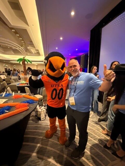 A man with a handlebar mustache poses with UTSA mascot Rowdy at a conference.