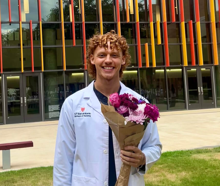 School of Nursing student Tyler Crow is featured with his white coat holding a bouquet of flowers after the School of Nursing's White Coat Ceremony.