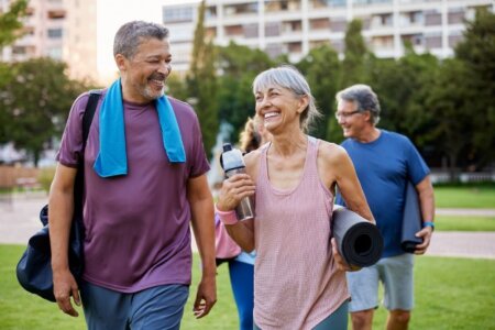 A woman carrying a yoga mat and water bottle talks with a man carrying a gym bag and wearing a towel around his neck.