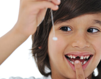 A smiling child holds up a baby tooth that just came out of his mouth.