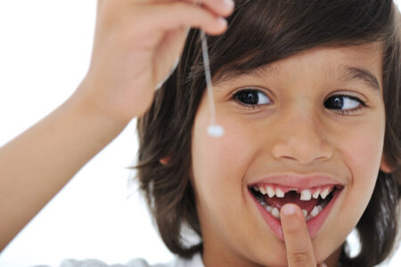 A smiling child holds up a baby tooth that just came out of his mouth.