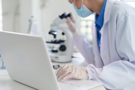 Scientist conducting medical research in a lab. Expert working on a laptop while observing through a microscope. Focus professional dedication.