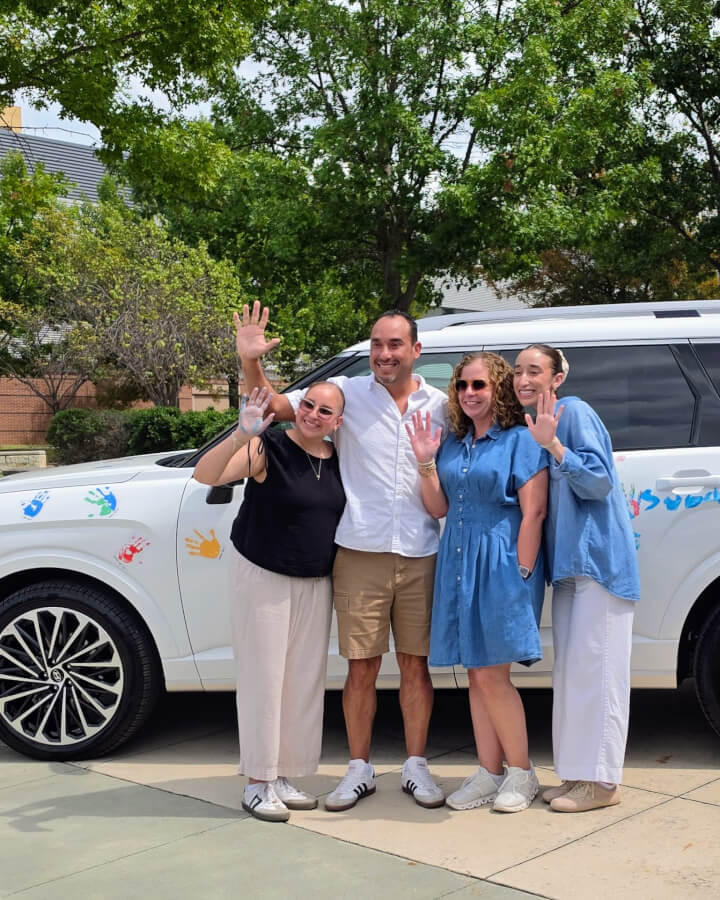 The Osorio family stand together and wave in front of a Hyundai SUV with painted handprints on it.