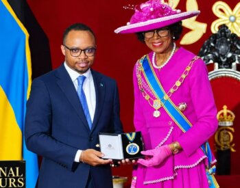 Man in a suit, Dr. Colton Jones, receives an award from a woman wearing a pink dress, Governor-General of the Bahamas Dame Cynthia Pratt.