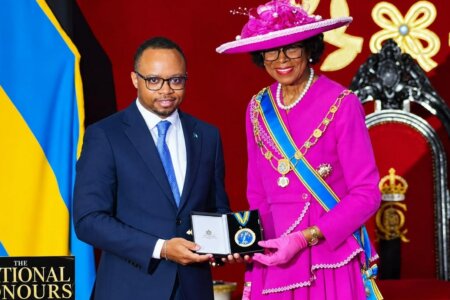 Man in a suit, Dr. Colton Jones, receives an award from a woman wearing a pink dress, Governor-General of the Bahamas Dame Cynthia Pratt.