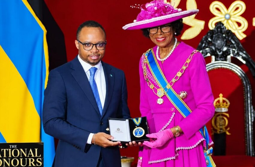 Man in a suit, Dr. Colton Jones, receives an award from a woman wearing a pink dress, Governor-General of the Bahamas Dame Cynthia Pratt.