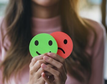 Woman Hands holding sad face hiding or behind happy smiley face, bipolar and depression, mental health concept, personality, mood change, therapy healing split concept.