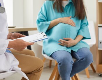 pregnant woman sitting at the desk in doctor's office visiting clinic. Health provider holding report file and giving consultation during medical exam