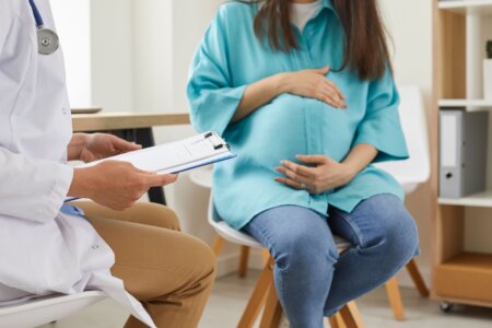 pregnant woman sitting at the desk in doctor's office visiting clinic. Health provider holding report file and giving consultation during medical exam