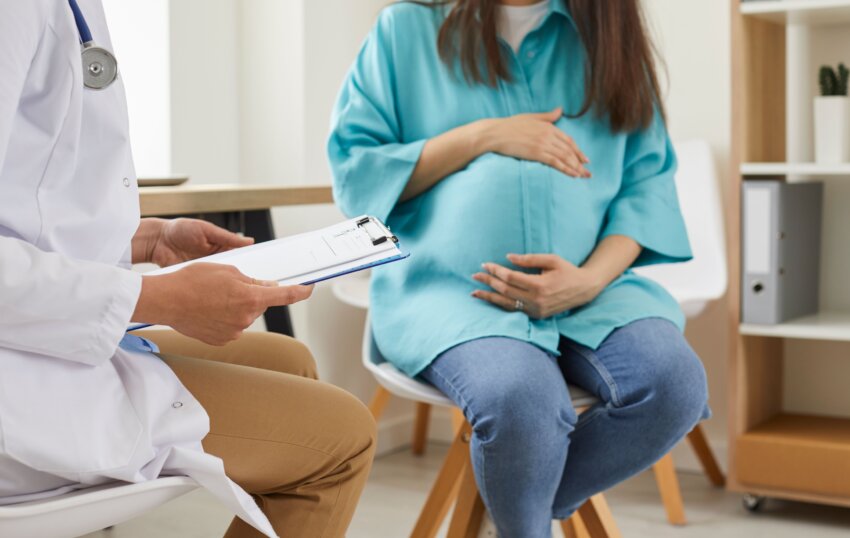 pregnant woman sitting at the desk in doctor's office visiting clinic. Health provider holding report file and giving consultation during medical exam