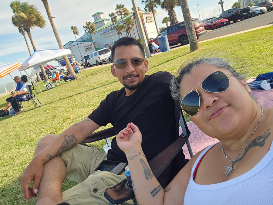 A Hispanic couple sitting next to the beach in their folding chairs.