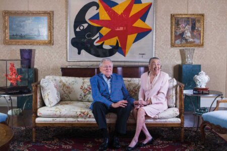 Joe R. and Teresa Lozano Long sit on a couch in front of a colorful painting.