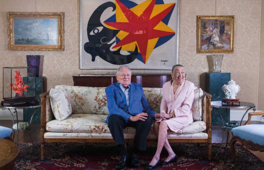 Joe R. and Teresa Lozano Long sit on a couch in front of a colorful painting.